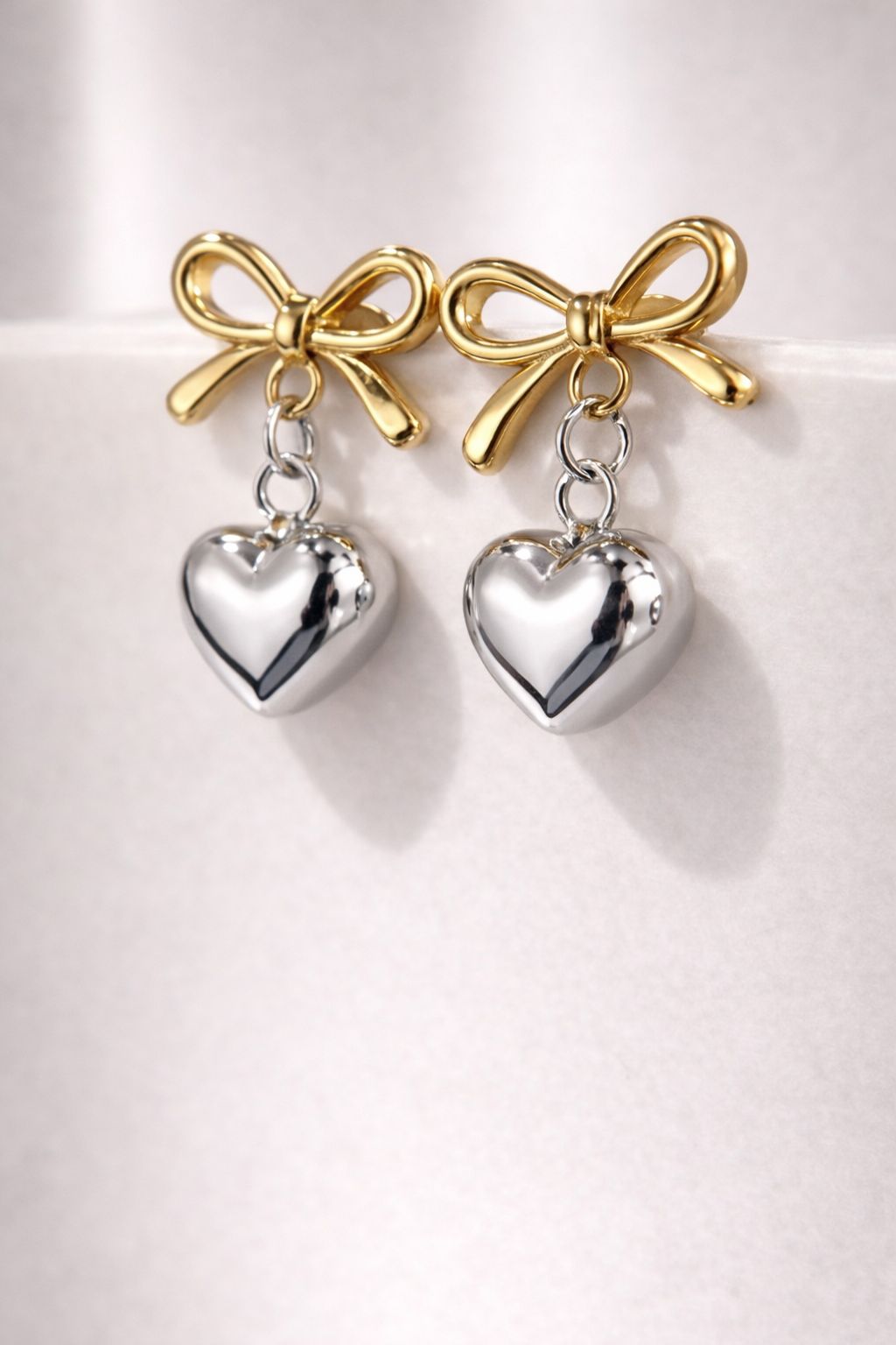 Pair of earrings with gold bows and silver heart charms on a white background